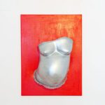 Gipsabdruck von einem Babybauch in Silber mit Rüschen an der Unterseite und dem Namen des Neugeborenen, präsentiert auf einer roten Leinwand