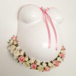 Ein weisser Gipsabdruck eines Babybauches von Brust und Bauch, gestaltet mit einer rosa Banderole und Schleife und einem Blumendekor an der Unterseite.