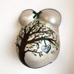 Ein 3D-Gipsabdruck eines Babybauches mit Brust und Bauch mit einer grünen Banderole und Schleife und gestaltet mit einem Lebensbaum an ein Herz das Bild der Babys zeigt.