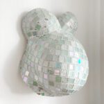 Ein Gipsabdruck eines Babybauches mit Brust und Bauch besetzt mit vielen Mosaiksteinen in grünen, blauen, weissen und rosa Pastellfarben.