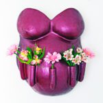 Ein Gipsabdruck eines Babybauches mit Brust und Bauch in Lila mit fünf Blumenhaltern auf der Vorderseite des Bauches in denen Blumen stecken.