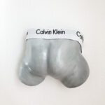 Ein Gipsabdruck von einen Babypo eines neugeborenen Babys in der Gestaltung einer Calvin Klein Boxershort in den Farben Silber und Weiss.